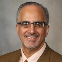 Portrait of a researcher in a suit and glasses, smiling against a neutral background.