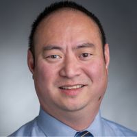 Portrait of a smiling male researcher in a blue dress shirt and tie.