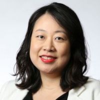 Portrait of a smiling researcher with dark hair and red lipstick, wearing a white blazer.