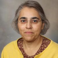 Portrait of a researcher wearing a yellow cardigan and glasses, smiling gently at the camera.