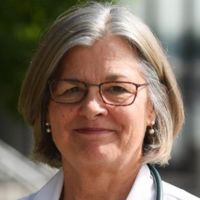 Portrait of a female researcher in a lab coat with glasses and a warm smile.