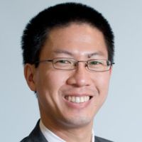 Portrait of a smiling researcher with glasses and short black hair, wearing a suit and tie.